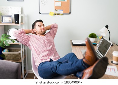Handsome young guy with his feet up on his office desk and arms behind the head. Man on his 20s looking relaxed because he finished working