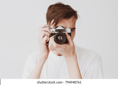 A Handsome Young Guy, Taking Pictures Of A Soviet, Old Mirror Camera. A Man Is Dressed In A White Jersey On A White Background.