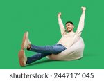 Handsome young happy man resting on beanbag chair against green background