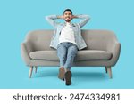 Handsome young happy man resting on sofa against blue background