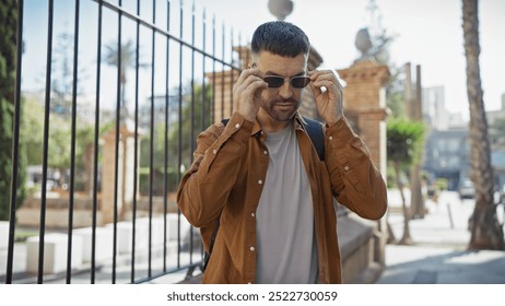 Handsome young hispanic man adjusting sunglasses outdoors in a sunny urban setting - Powered by Shutterstock