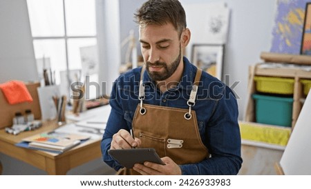 Handsome young hispanic man, ardently immersed in art, passionately drawing on a touchpad in art studio offering an intimate glimpse into a creative journey.