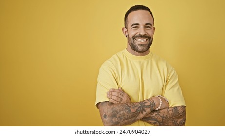 Handsome young hispanic man with beard and tattoos posing confidently against a vibrant yellow background. - Powered by Shutterstock