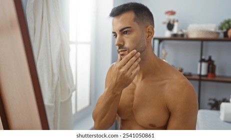 Handsome young hispanic man with a beard examining his reflection in a spa or salon room, showcasing a wellness setting with indoor beauty elements. - Powered by Shutterstock