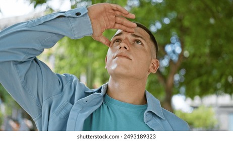 Handsome young hispanic man outdoors looking upward, casual and attractive in an urban park setting. - Powered by Shutterstock