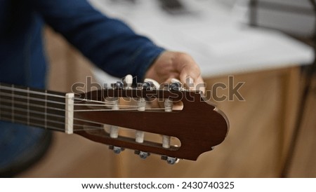 Handsome young hispanic man passionately tuning his classical guitar, setting the stage for a melodic performance in the heart of a cozy music studio