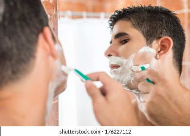 Handsome Young Hispanic Man Shaving In Front Of A Mirror