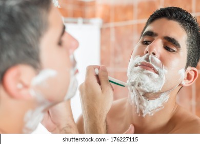 Handsome Young Hispanic Man Shaving In Front Of A Mirror