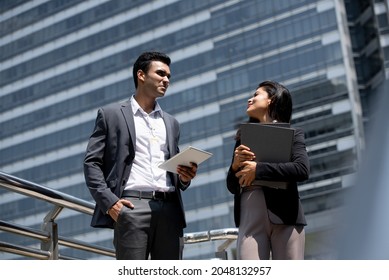 Handsome young Indian businessman in corporate wear talking with businesswoman outdoors in the city