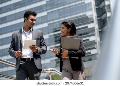 Handsome young Indian businessman in formal suit talking with businesswoman outdoors in the city