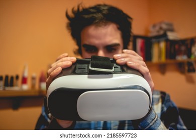 Handsome Young Latino Man With Plaid Shirt Holding A Virtual Reality Helmet (VR Glasses) In Orange Bedroom On Home