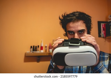 Handsome Young Latino Man With Plaid Shirt Holding A Virtual Reality Helmet (VR Glasses) In Orange Bedroom On Home