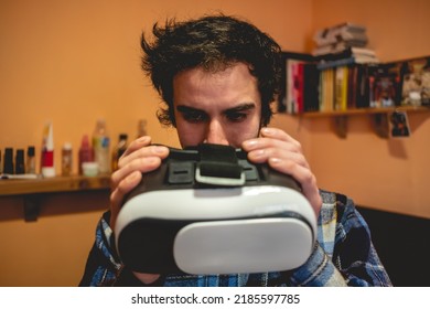 Handsome Young Latino Man With Plaid Shirt Holding A Virtual Reality Helmet (VR Glasses) In Orange Bedroom On Home