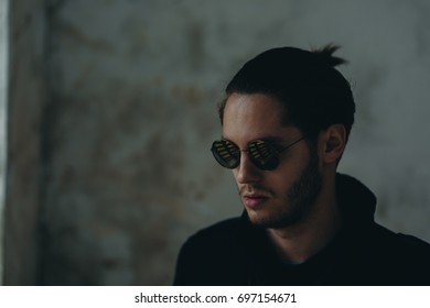 Handsome Young Looking Guy Wearing Black Jacket And Sunglass. There Is Reflection Of The Windows In The Sunglasses. Slight Beard With Little Moustache. Pony Tail On Backside Is Visible.