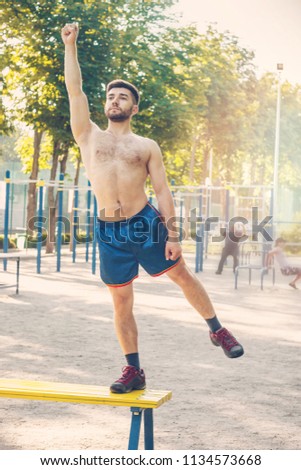 Handsome young male athlete standing on bench in sports playground, hand up, like superman, retro effect