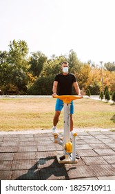 Handsome Young Male Caucasian Athlete With Face Mask Trains On Arm And Leg Equipment In An Outdoor Gym. Muscular Athlete Outdoors. COVID - 19 Coronavirus Protection