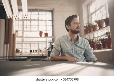 Handsome young male small business owner sitting in his studio workshop thinking positively while looking away into the distance - Shutterstock ID 324738998