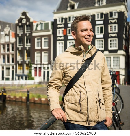 Handsome young man, admiring the beauty of Amsterdam center on a bridge in a sunny summer day