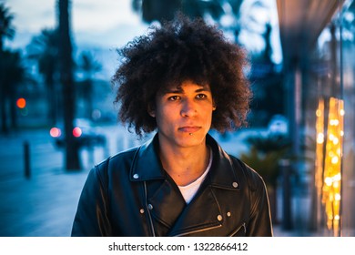 Handsome young man with afro hair illuminated by yellow light of a showcase looking seriously with urban background in blue tones - Powered by Shutterstock