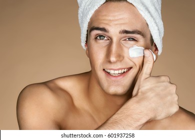Handsome young man applying cream to his face. Portrait of a smart man with perfect skin. Skin care concept