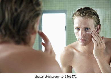 Handsome Young Man Applying Moisturiser Cream In Front Of Mirror