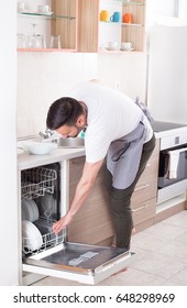 Handsome Young Man With Apron Unloading Dishwasher Husband Doing Chores Handsome Young Man With Apron Unloading Dishwasher Husband Doing Chores