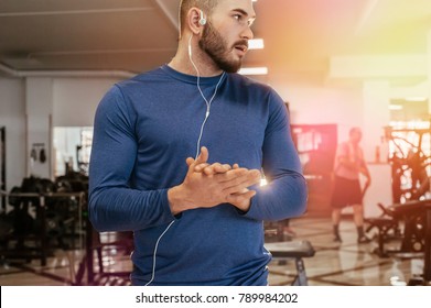 A Handsome Young Man Athlete Trains In The Gym. The Man Talking On The Phone With Headphones. The Guy Listens To Music In White Headphones