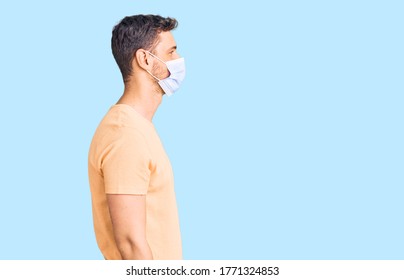 Handsome Young Man With Bear Wearing Medical Mask For Coronavirus Looking To Side, Relax Profile Pose With Natural Face With Confident Smile. 