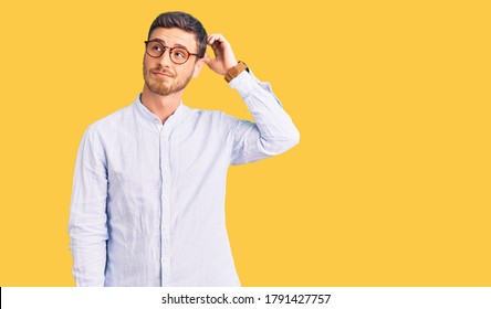 Handsome young man with bear wearing elegant business shirt and glasses confuse and wondering about question. uncertain with doubt, thinking with hand on head. pensive concept. 