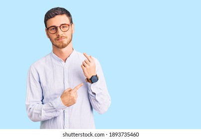Handsome young man with bear wearing elegant business shirt and glasses in hurry pointing to watch time, impatience, looking at the camera with relaxed expression 