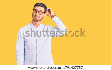 Handsome young man with bear wearing elegant business shirt and glasses confuse and wondering about question. uncertain with doubt, thinking with hand on head. pensive concept. 