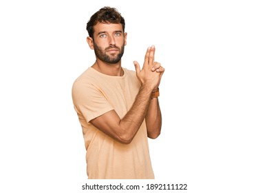 Handsome Young Man With Beard Wearing Casual Tshirt Holding Symbolic Gun With Hand Gesture, Playing Killing Shooting Weapons, Angry Face 