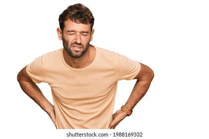 Handsome Young Man With Beard Wearing Casual Tshirt Suffering Of Backache, Touching Back With Hand, Muscular Pain 