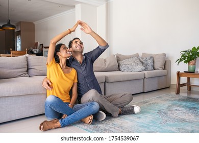 Handsome young man with beautiful indian woman dreaming a new home. Smiling married couple moves to new apartment with copy space. Happy middle eastern couple making roof with hands symbol of new home