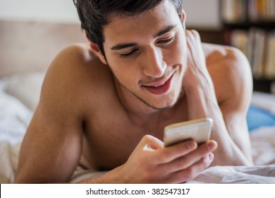 Handsome Young Man In Bed Typing On Cell Phone