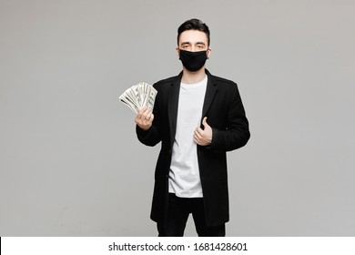 Handsome Young Man In Black Protective Mask Holding A Pack Of Money, Isolated On Grey Background With Copy Space. Concept Of Medical And Pharmaceutical Business In A Season Of Flu And World Pandemic