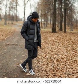 Handsome Young Man In A Black Winter Jacket And Knitted Hat In The Park.