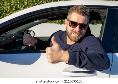 Handsome young man in a blue sweater driving a car showing thumb up.