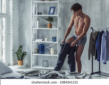 Handsome Young Man In Boxer Briefs Is Pulling On His Pants While Getting Dressed At Home