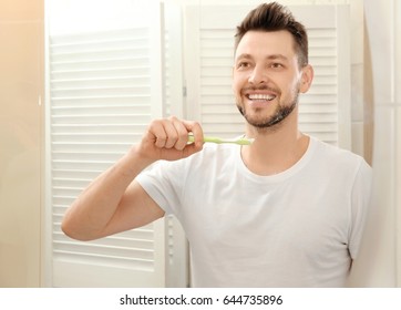 Handsome Young Man Brushing Teeth And Looking In Mirror