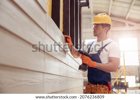 Handsome young man builder installing exterior wood siding