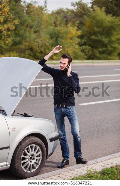 Handsome young man calling for assistance with\
his car broken down by the\
roadside