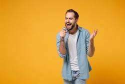 Handsome Young Man In Casual Blue Shirt Posing Isolated On Yellow Orange Wall Background, Studio Portrait. People Lifestyle Concept. Mock Up Copy Space. Sing Song In Microphone, Keeping Eyes Closed
