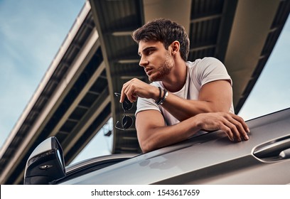 Handsome Young Man In Casual Clothes Standing Near His Modern Sport Car On The Street