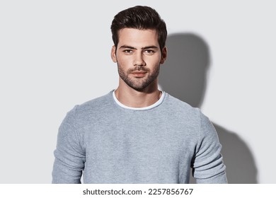 Handsome young man in casual wear looking at camera while standing against grey background