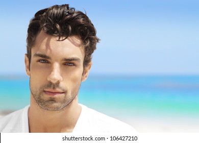 Handsome young man in casual white top against bright beach background