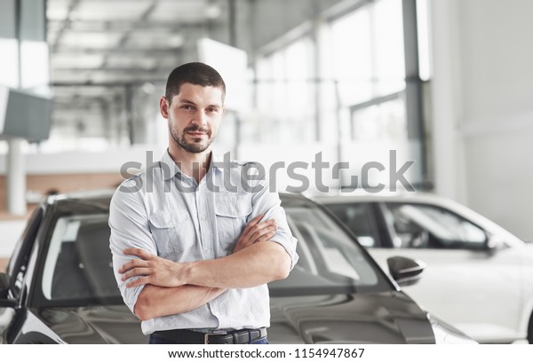 Handsome young man consultant at car salon standing\
near car