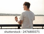Handsome young man with cup of delicious latte by the waterfront, back view