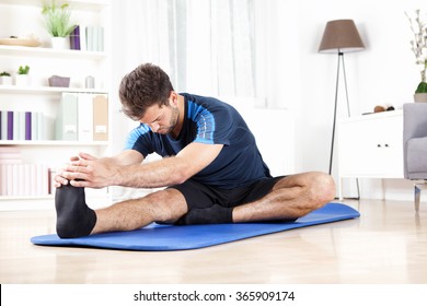 Handsome Young Man Doing Hamstring Stretch Exercise On Top Of A Mat At Home.