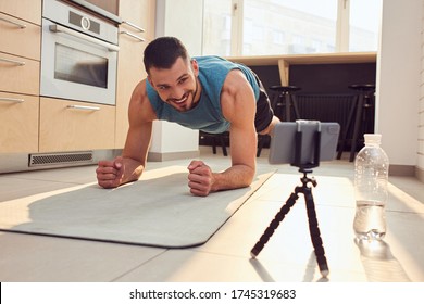 Handsome Young Man Doing Plank Exercise And Chatting With Instructor Online During Morning Training